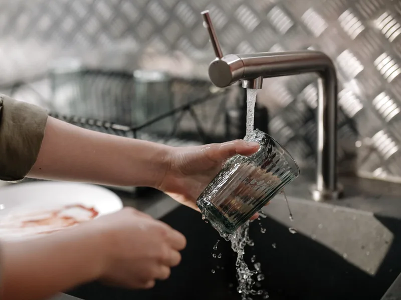 Clear water flowing from a kitchen faucet over a drinking glass